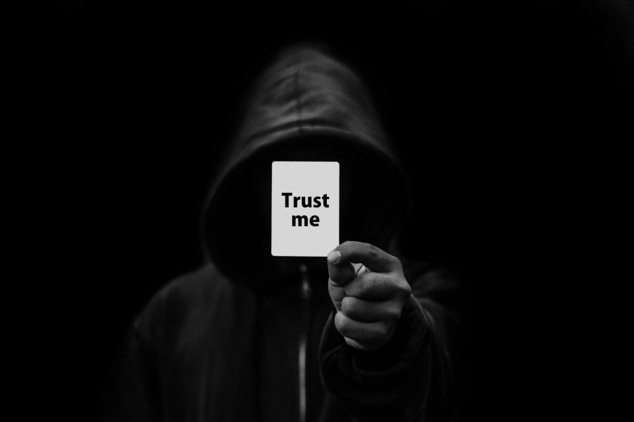 A hooded figure holding a card that says Trust Me | Image by Gerd Altmann from Pixabay