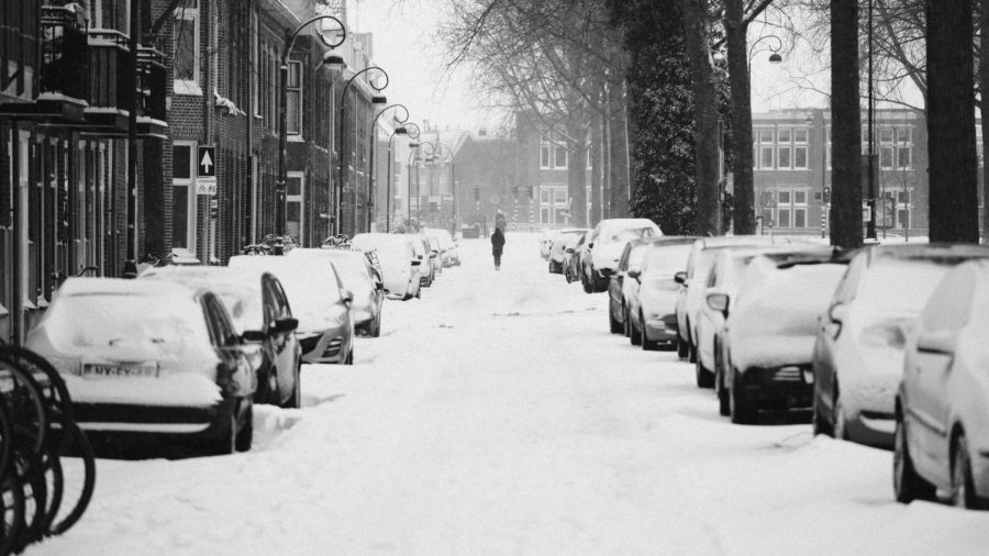 Someone walking on a snowy street after a snowstorm with cars parked on it. | Photo Credit: Photo by Marc Kleen on Unsplash