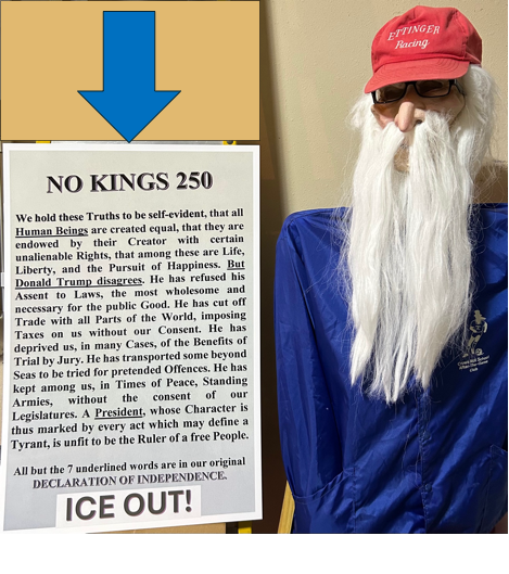 A sign from a No Kings protest next to a mannequin wearing a mask, blue jacket, and red hat.